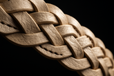 Close-up detail of beige braided leather belt with dark background